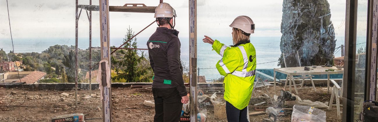 Deux experts Apave en casque de chantier observant l'extérieur depuis une baie vitrée en travaux