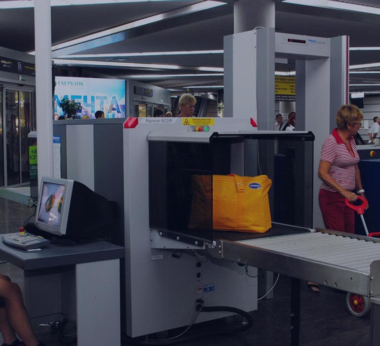 femme en train d'inspecter des bagages au niveau d'un portique de sécurité à l'aéroport