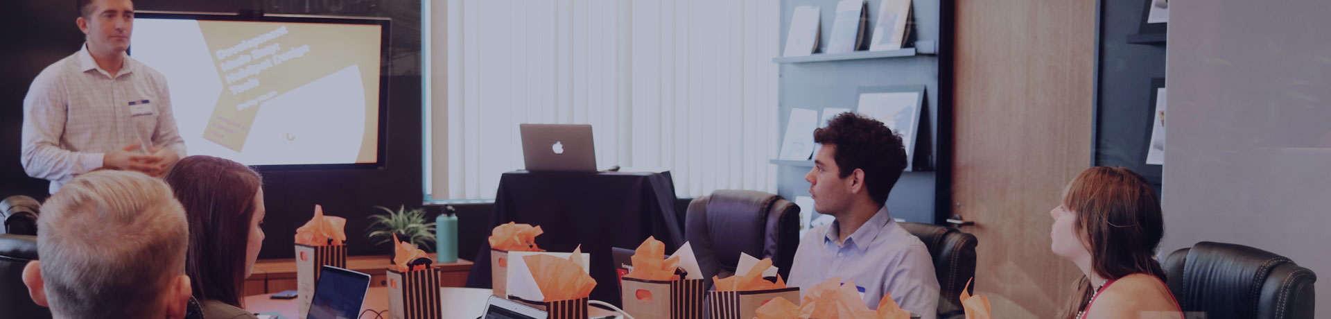 Un homme présente devant tout le monde autour d'une table devant leur ordinateur