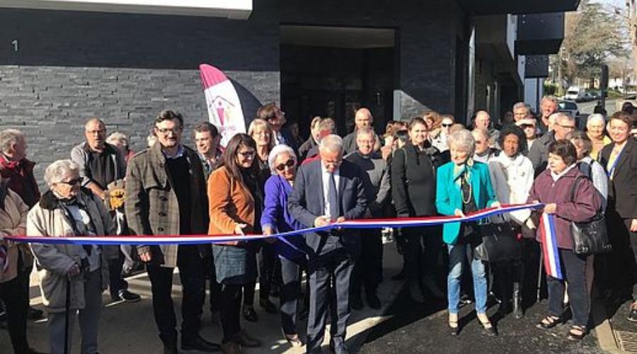 Un groupe de personnes se réunissant pour une inauguration, une personne coupe un ruban
