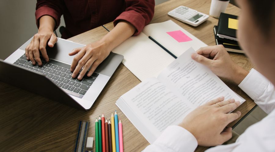 Two pairs of student hands: one typing on a keyboard, the other reading a book
