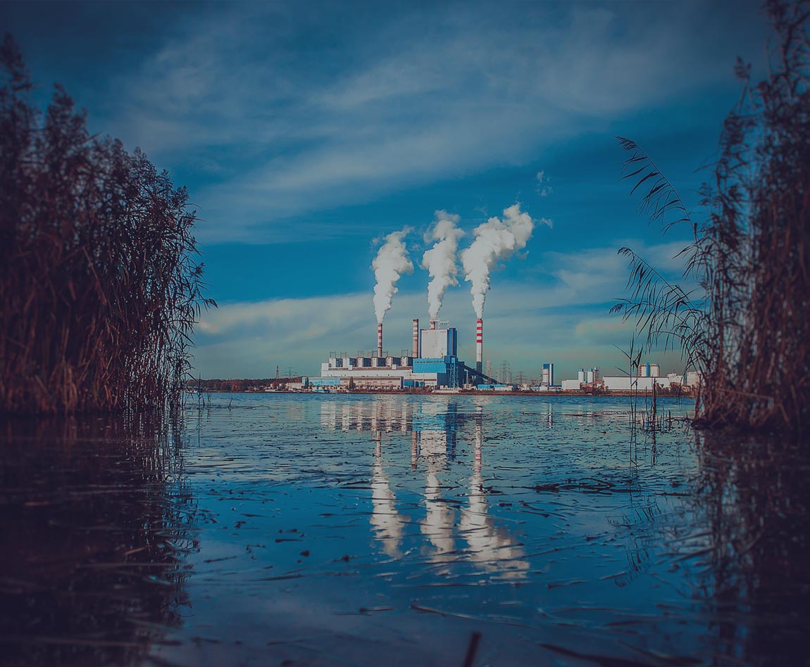 factory with 3 smoke columns in front of a lake