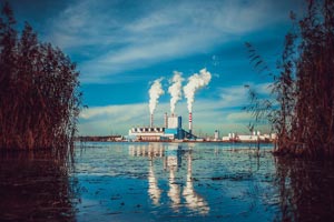 fábrica con 3 columnas de humo frente a un lago