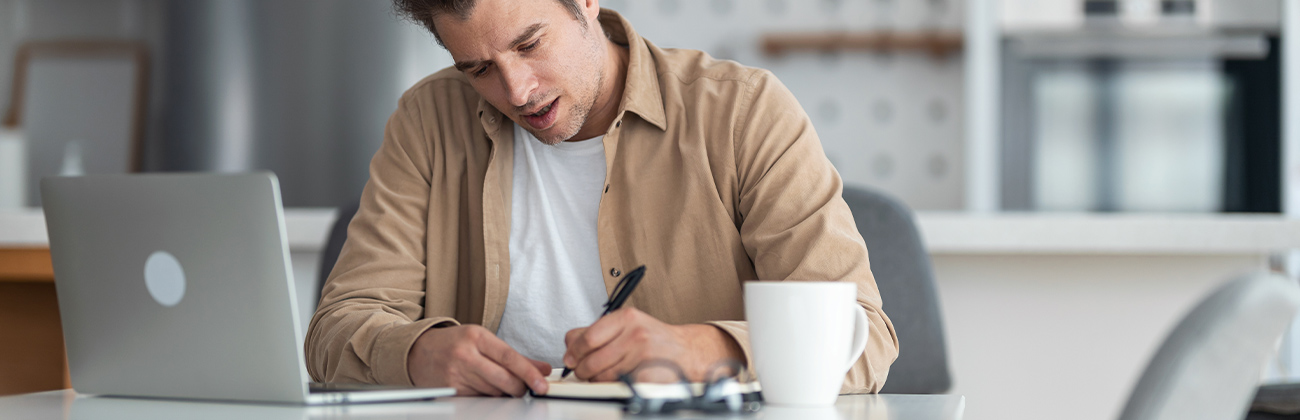 Homme d'âge moyen prenant des notes tout en suivant un cours en ligne.