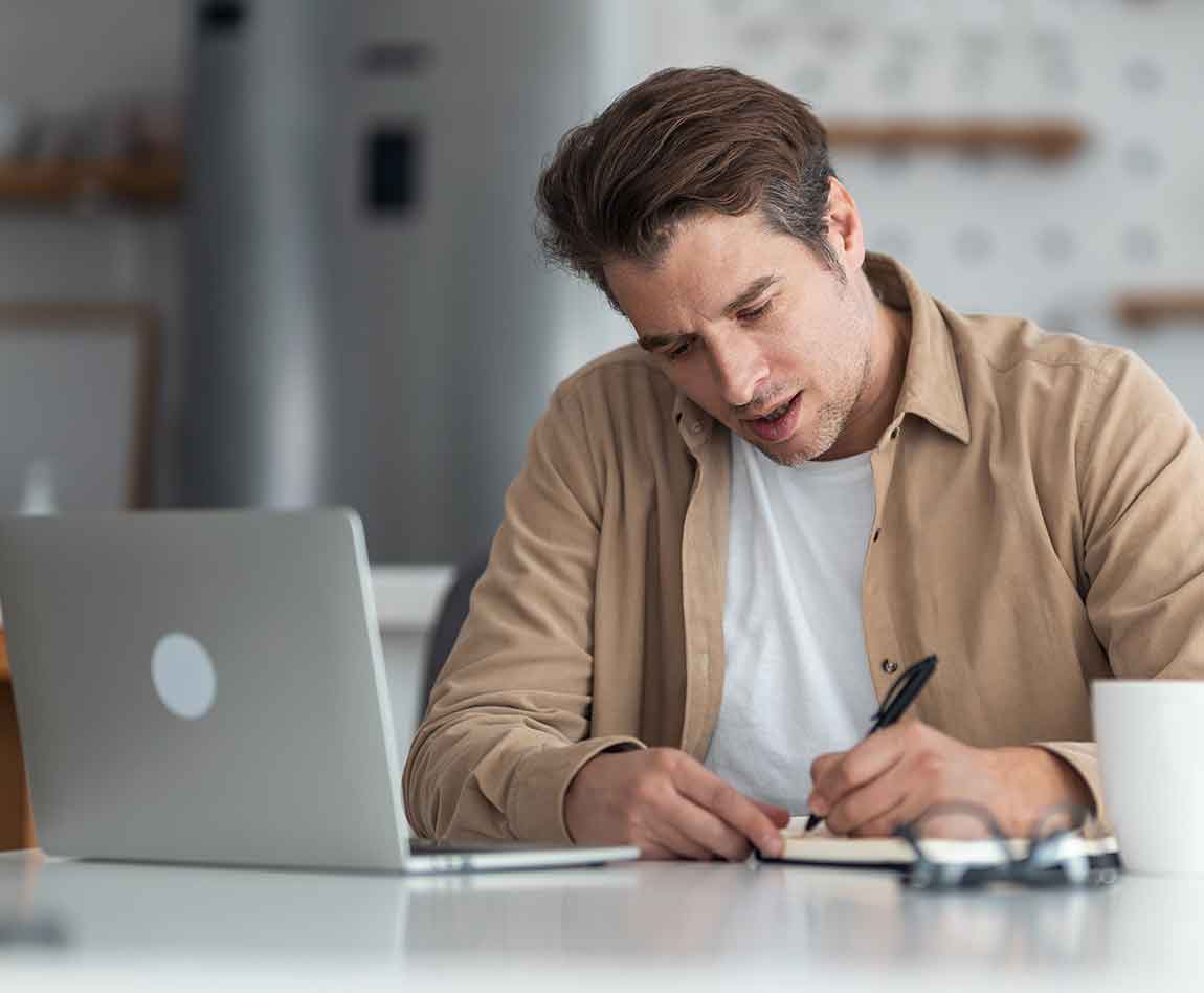 Homme d'âge moyen prenant des notes tout en suivant un cours en ligne.
