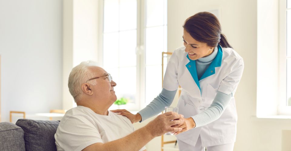 Une aide soignante donne un verre d'eau à un monsieur âgé
