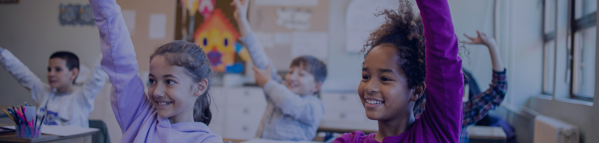 Des écoliers dans une salle de classe, les mains levées, répondent aux questions de l'enseignant et sourient.