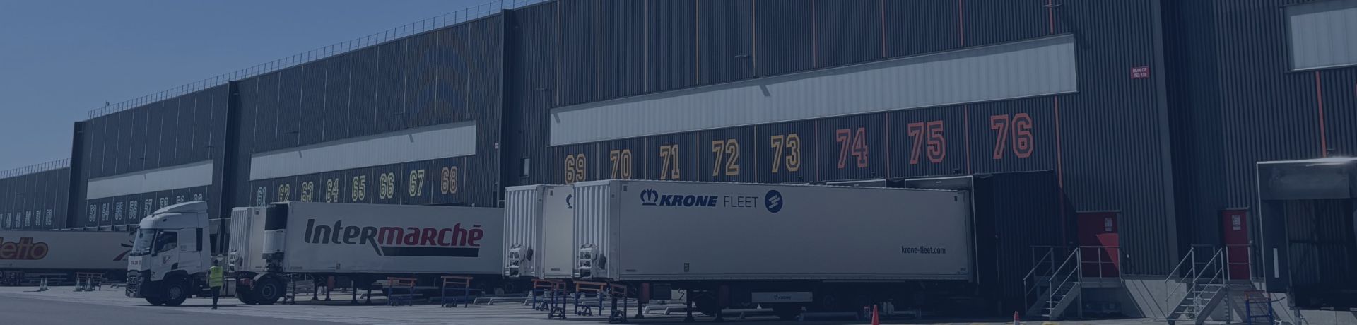 Quai de chargement logistique avec camions Intermarché devant un grand entrepôt.