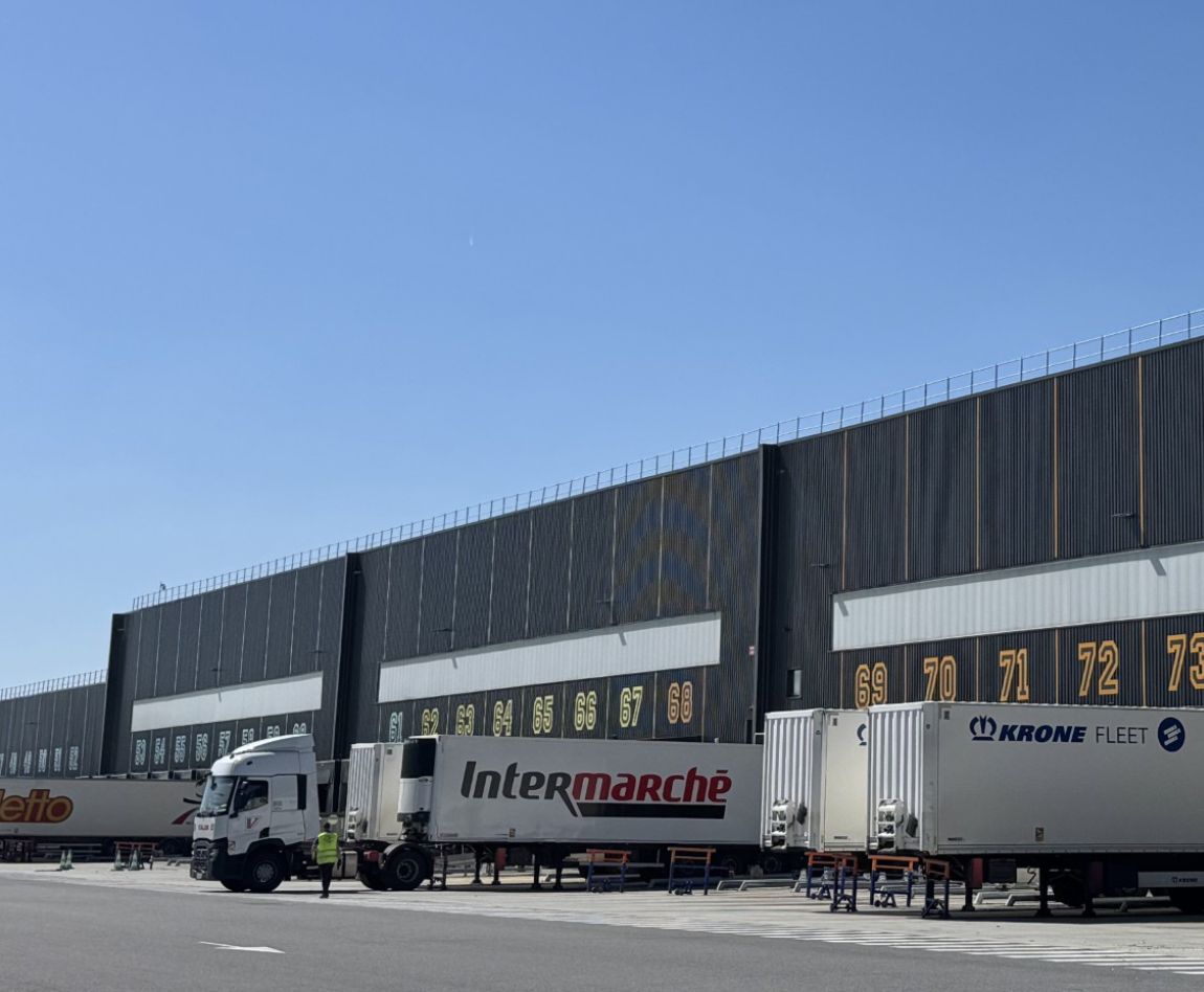 Quai de chargement logistique avec camions Intermarché devant un grand entrepôt.