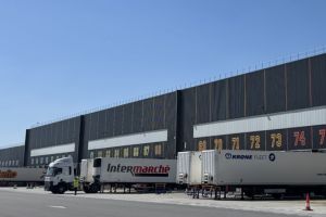 Quai de chargement logistique avec camions Intermarché devant un grand entrepôt.