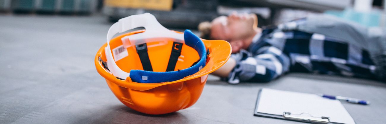 Travailleur blessé au sol dans un entrepôt, casque de sécurité à proximité.