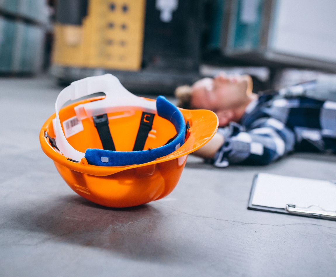 Travailleur blessé au sol dans un entrepôt, casque de sécurité à proximité.