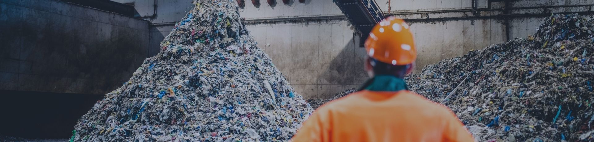 Opérateur en gilet orange observant un monticule de déchets triés sous un tapis convoyeur.
