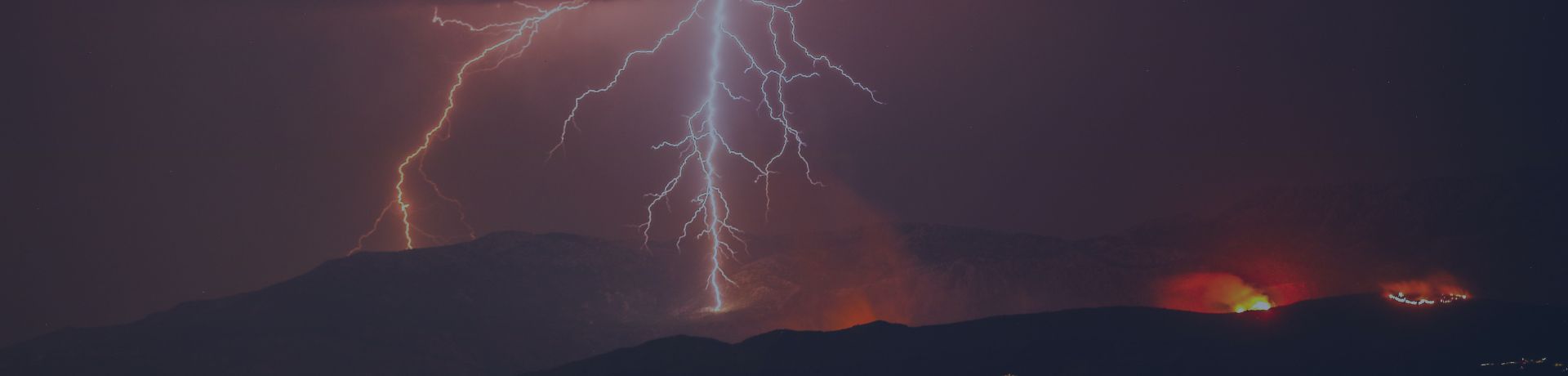 Éclairs frappant une montagne au-dessus d'une ville côtière illuminée de nuit.