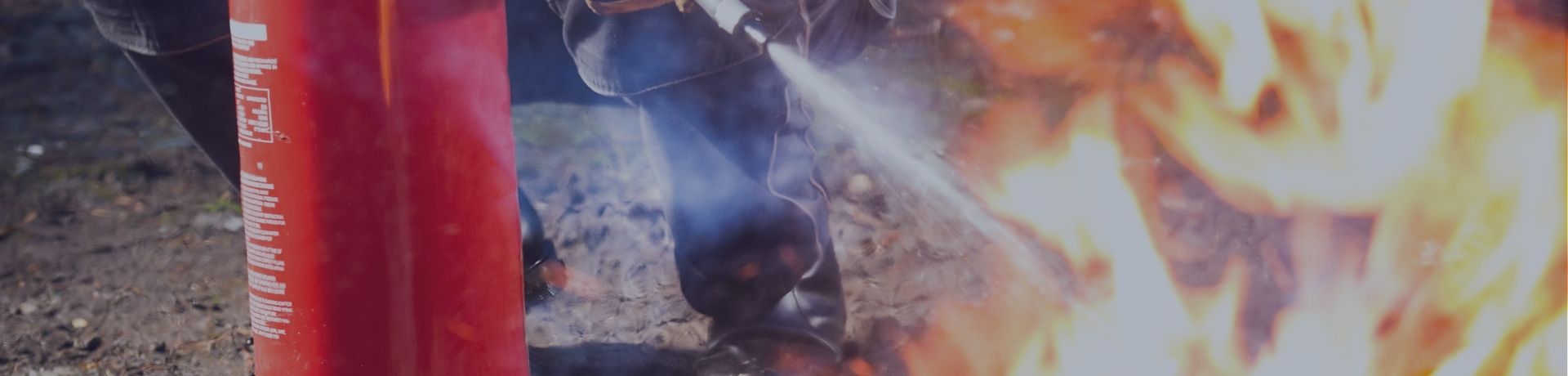 Personne équipée de gants manipulant un extincteur rouge pour éteindre un foyer de flammes.