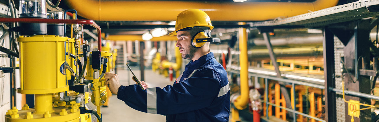 Jeune travailleur en tenue de protection à l'aide d'une tablette lors de la vérification des machines dans l'usine de chauffage.