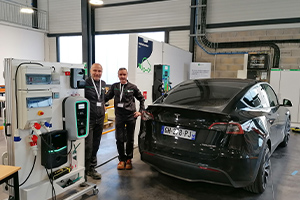 Deux collaborateurs Apave devant une voiture Tesla et un table