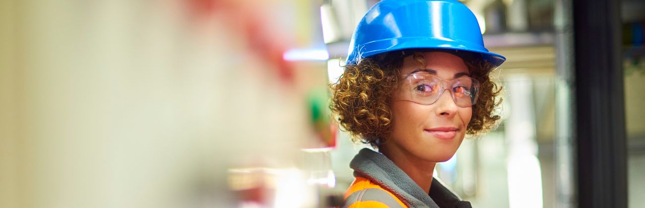 Une femme technicienne avec un gilet orange et un casque de protection bleu