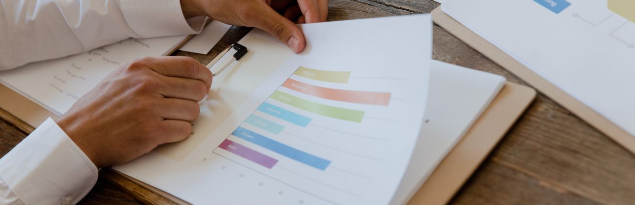 Gros plan sur des mains examinant un graphique à barres en couleurs, posé sur un bureau en bois, illustrant une analyse de données.