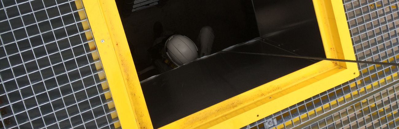 Une trappe d'accès jaune ouverte avec une échelle métallique qui descend vers un espace confiné.