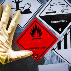 Main gantée pointant des étiquettes de danger chimique (inflammable, corrosif
