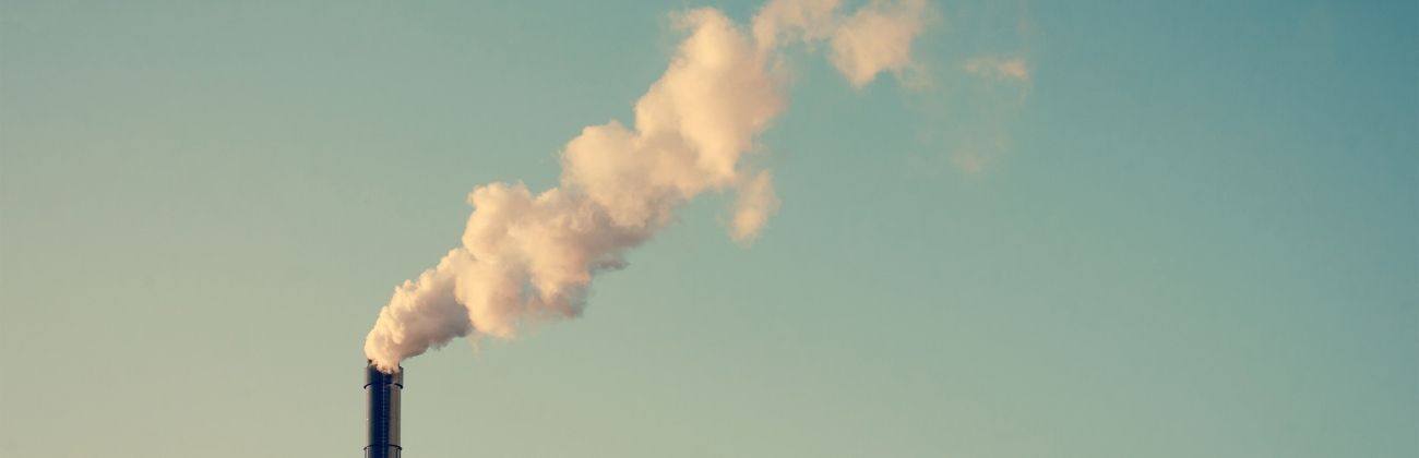 Fumée blanche s'échappant d'une grande cheminée industrielle sur fond de ciel bleu.