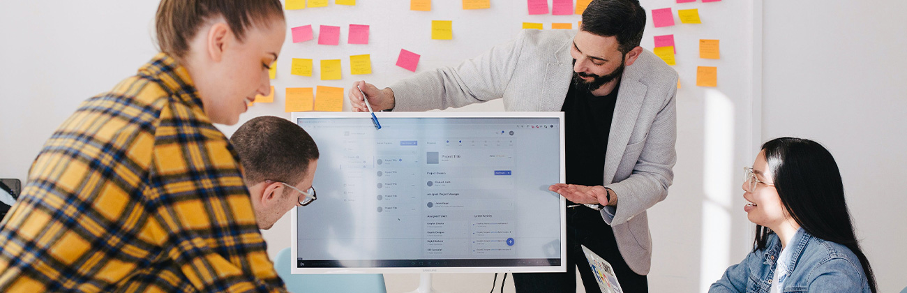 Un homme debout derrière un écran plat d'ordinateur entouré de son équipe