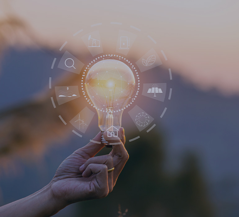 Main tenant une ampoule avec des pictogrammes représentant des sources d'énergie renouvelables