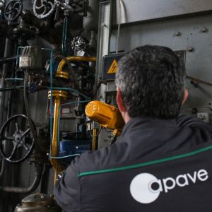 Gros plan sur un travailleur de dos, en combinaison de travail, inspectant une valve industrielle et des tuyaux.