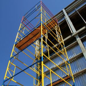 Une vue en contre-plongée d'un échafaudage en métal jaune et bleu devant un bâtiment moderne à la façade métallique.