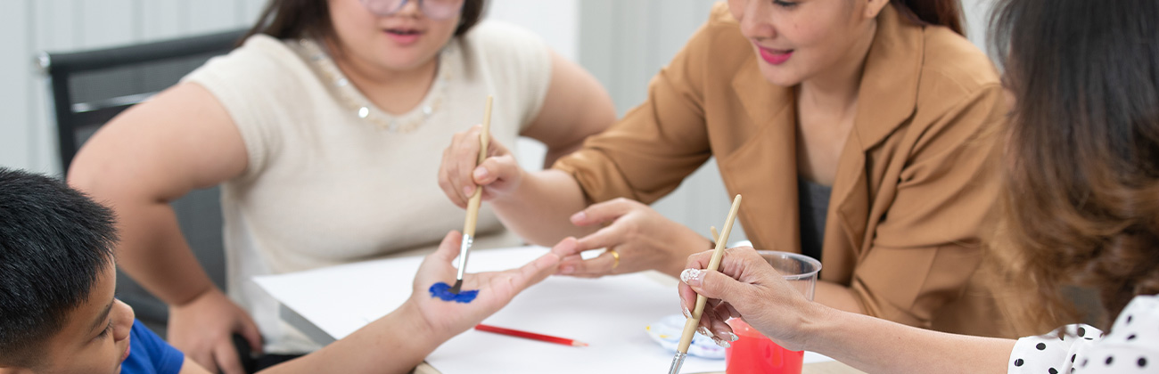 Une dame aide des enfants handicapés, ils font de la peinture