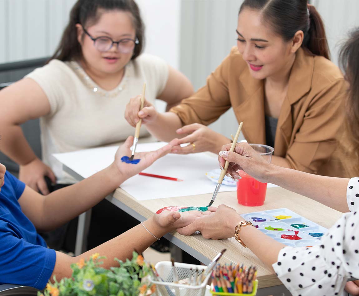 Une dame aide des enfants handicapés, ils font de la peinture