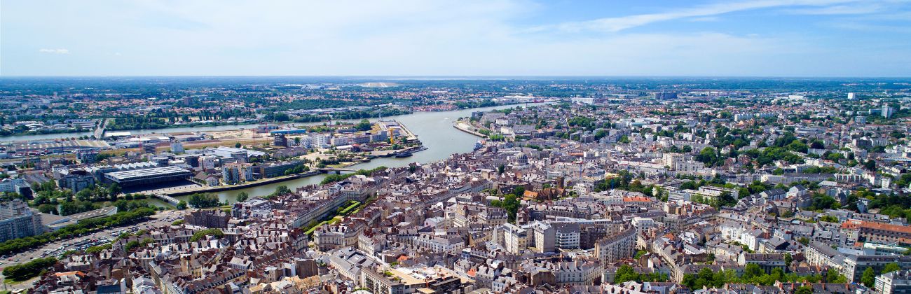Vue aérienne panoramique d'une ville dense traversée par un fleuve sous un ciel bleu.
