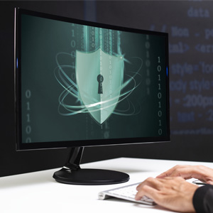  Un gros plan sur un écran d'ordinateur affichant un bouclier avec une serrure, symbolisant la cybersécurité, avec des mains tapant sur un clavier au premier plan.