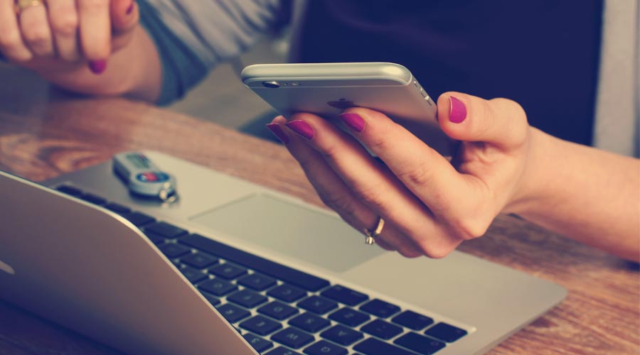 donna al computer con uno smartphone in mano
