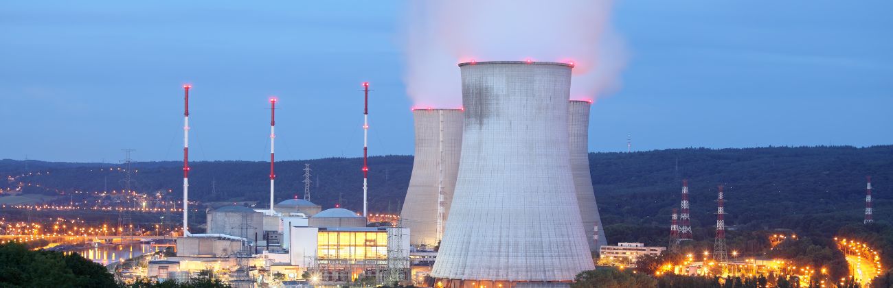 Nuclear power plant with cooling chimneys and reactors, illuminated at night.