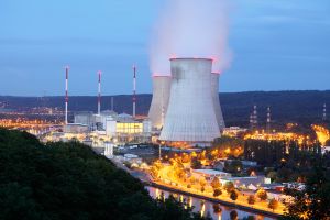 Nuclear power plant with cooling chimneys and reactors, illuminated at night.