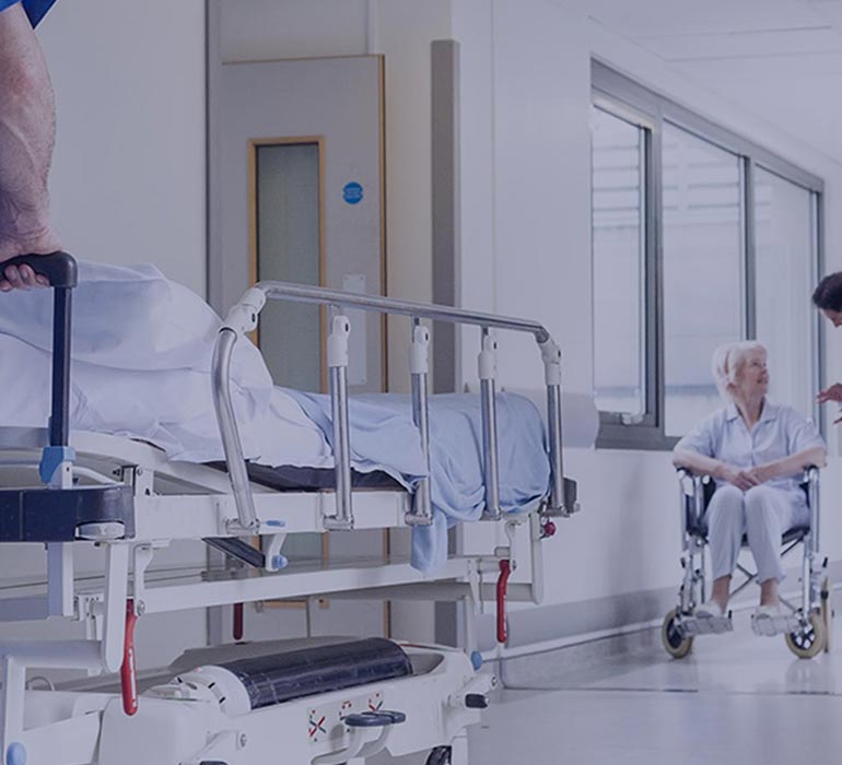 In a hospital corridor, a man pushes a medical bed
