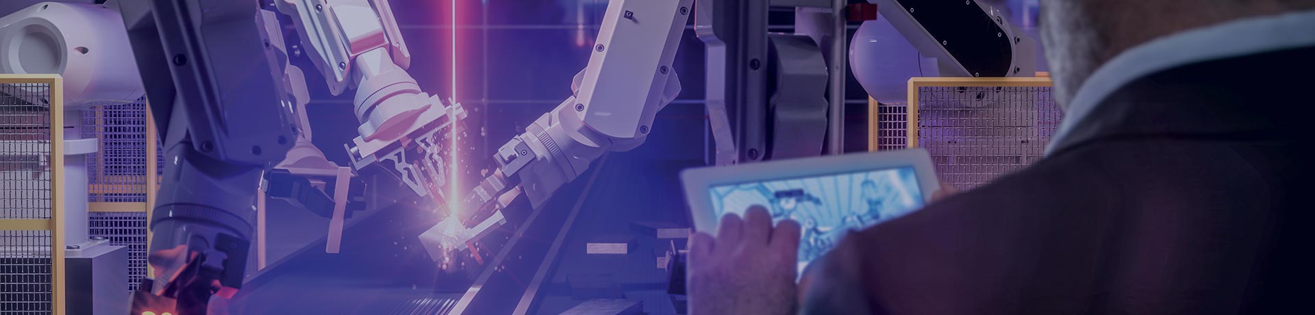 Un homme tient une tablette dans ses mains face à des bras robots