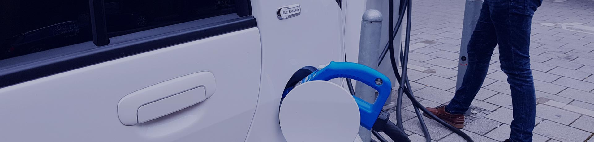 Un homme en train de brancher sa voiture électrique blanche sur une borne de recharge